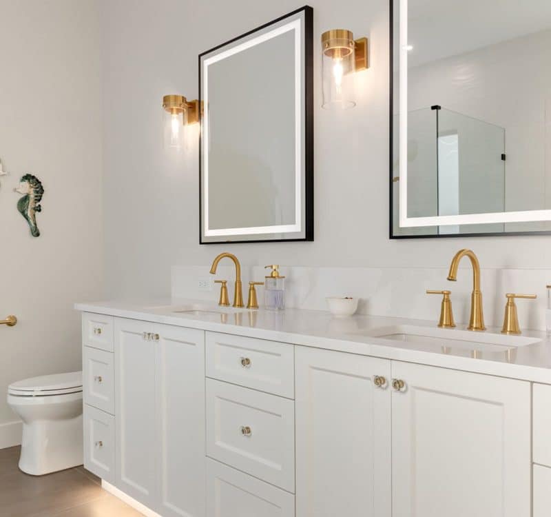 A modern bathroom featuring white cabinets and elegant gold fixtures, creating a stylish and bright atmosphere.
