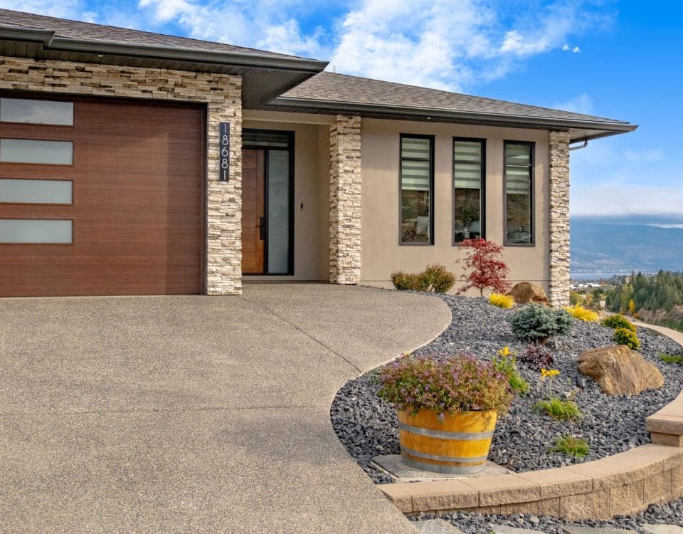 A house featuring a driveway leading to a garage, surrounded by a well-maintained lawn and landscaping.