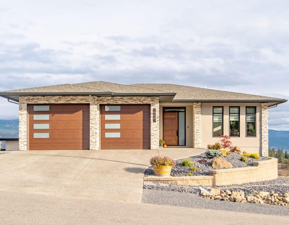 A house featuring a spacious driveway leading to a garage, surrounded by greenery and a clear blue sky.