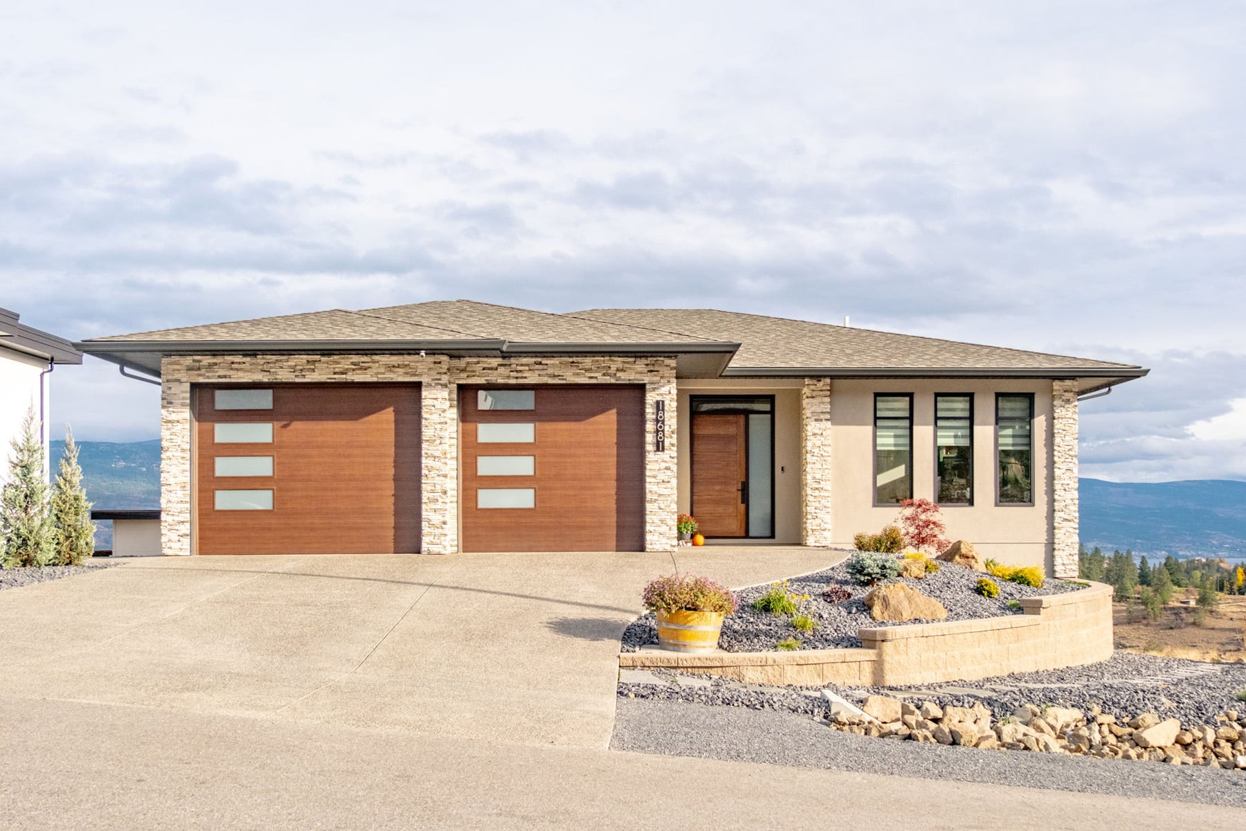 A house featuring a spacious driveway leading to a garage, surrounded by greenery and a clear blue sky.