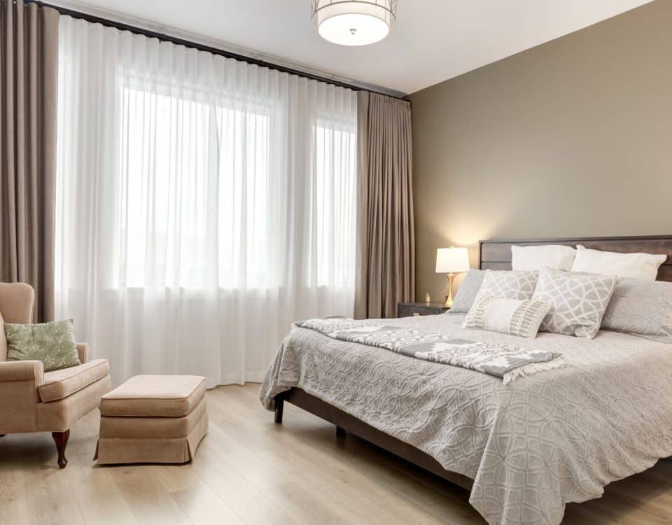 A cozy bedroom featuring a neatly made bed, a comfortable chair, and a bright window allowing natural light to enter.