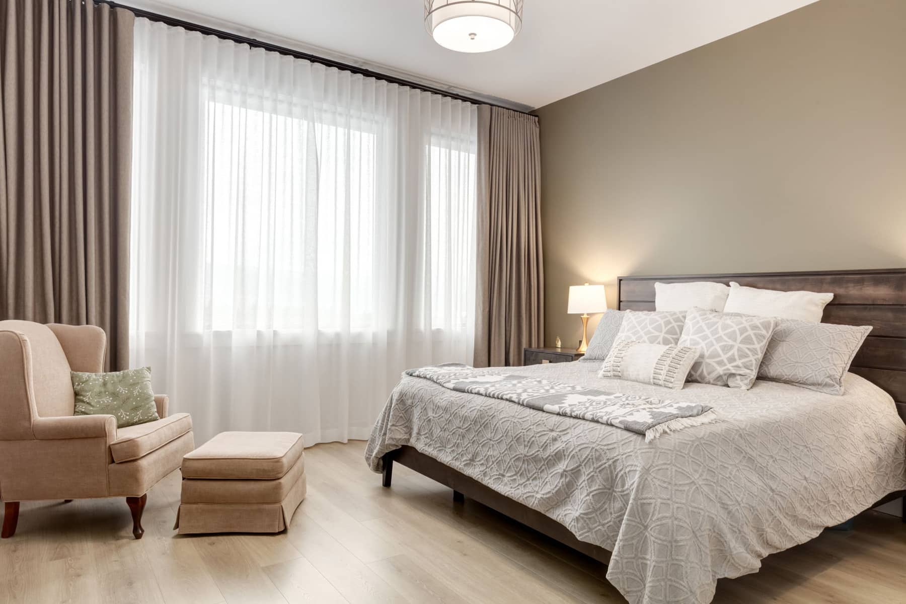 A cozy bedroom featuring a neatly made bed, a comfortable chair, and a bright window allowing natural light to enter.