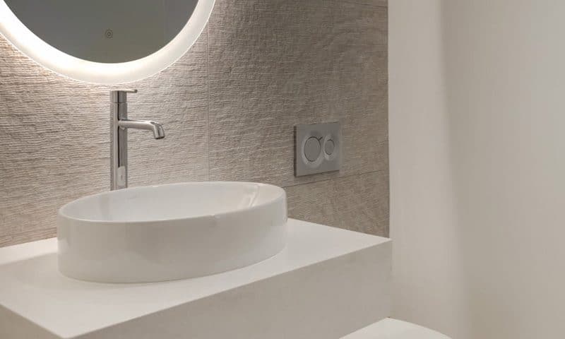 A modern bathroom featuring a round mirror above a sleek sink, showcasing contemporary design elements and clean lines.