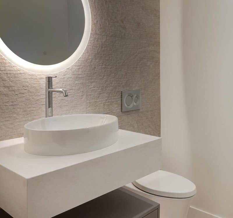 A modern bathroom featuring a round mirror above a sleek sink, showcasing contemporary design elements and clean lines.