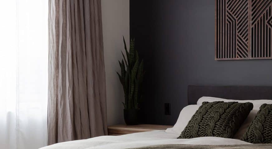 A modern bedroom featuring a black accent wall and a neatly made bed with decorative pillows.