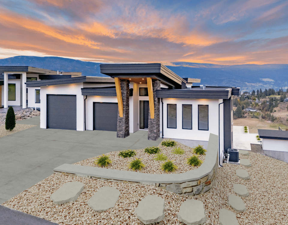 A house with a driveway and garage silhouetted against a vibrant sunset sky.