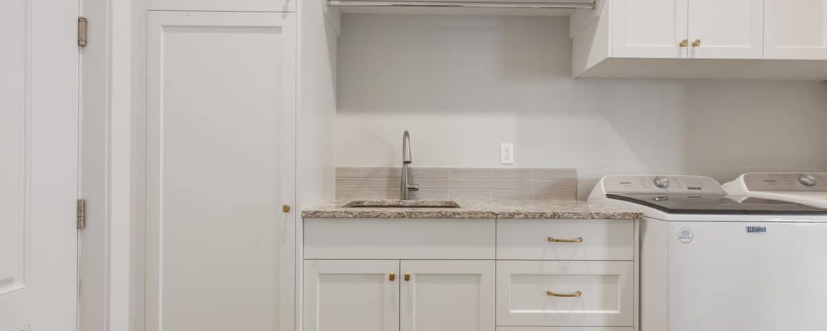 A bright white laundry room featuring a sink and a washing machine against a clean, minimalist backdrop.