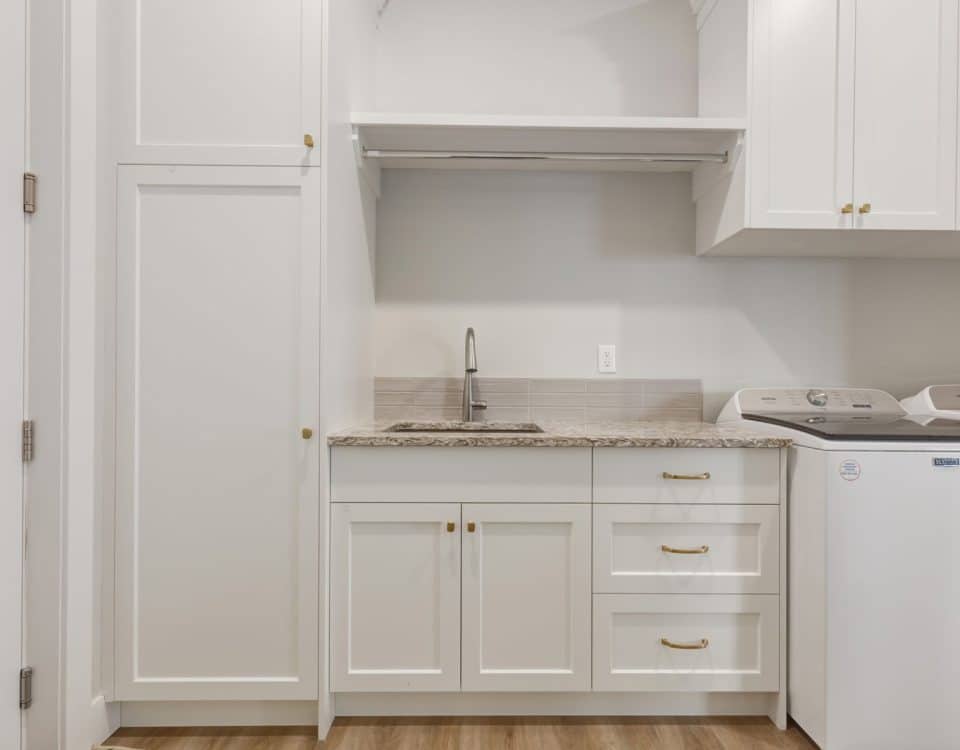 A bright white laundry room featuring a sink and a washing machine against a clean, minimalist backdrop.